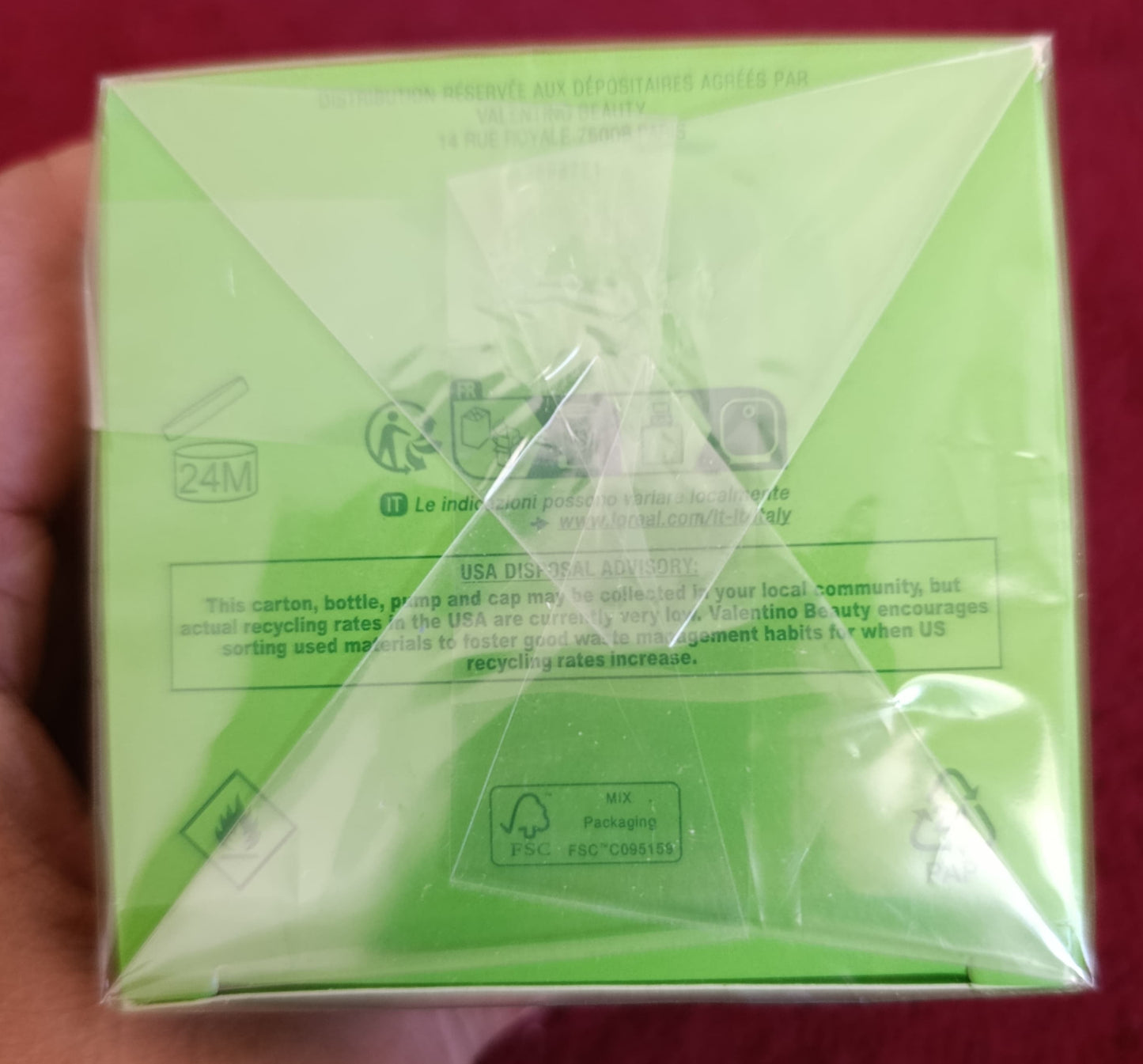 Green product packaging held in a hand against a red background