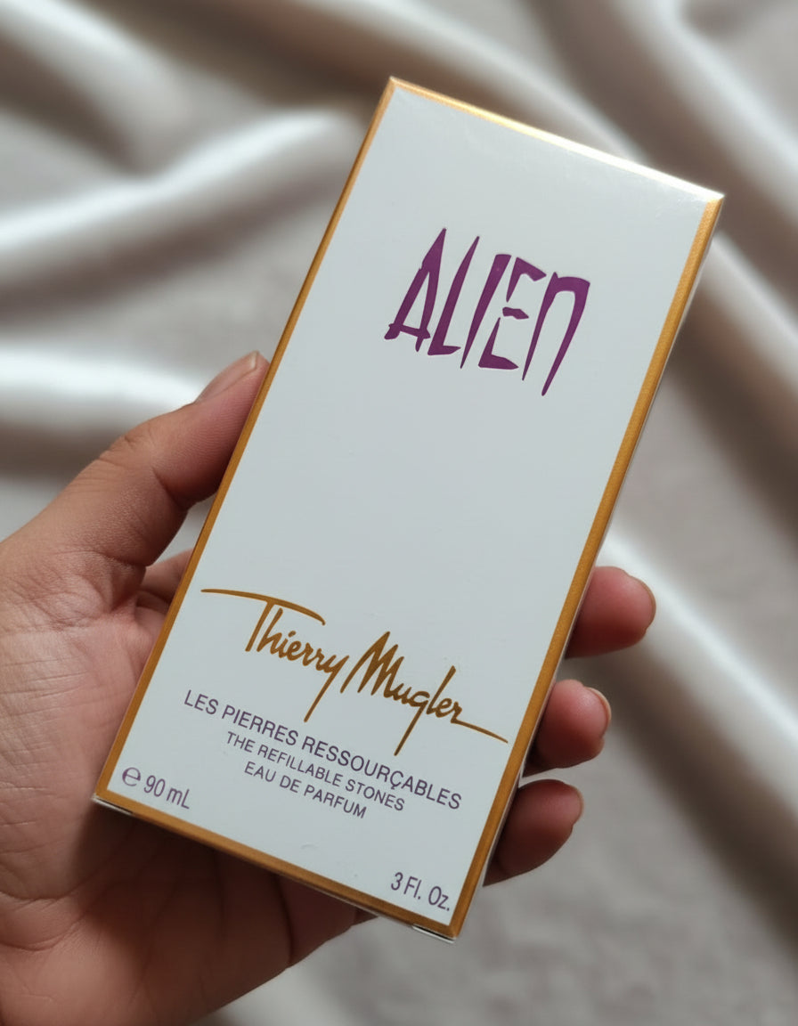 Thierry Mugler Alien perfume box held by a hand on a gray surface