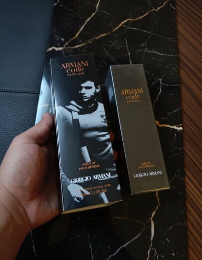 Two Armani Code perfume boxes held by a hand on a carpeted floor.
