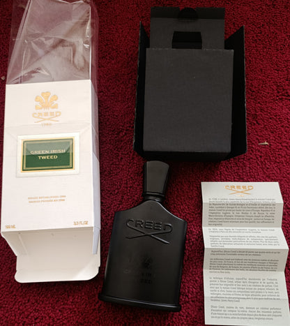 Black perfume bottle with packaging and papers on a red surface