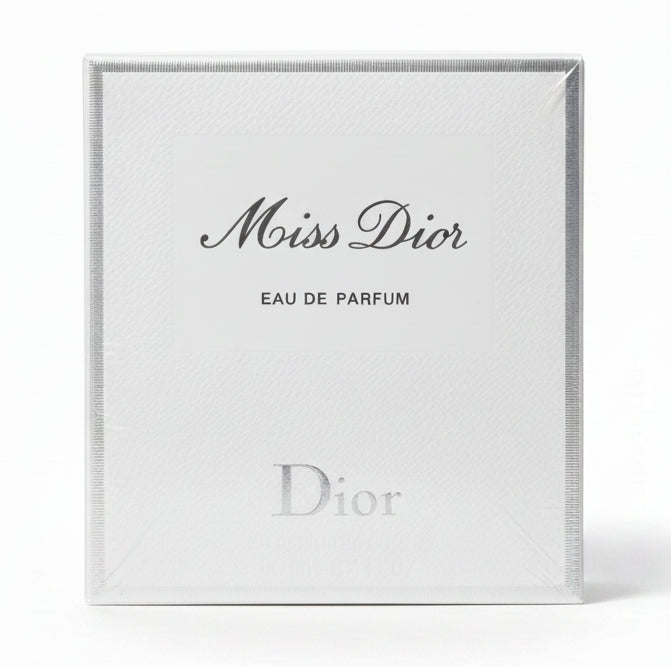 Miss Dior Eau de Parfum packaging held by a hand on a red background