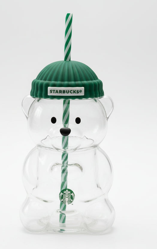 Clear bear-shaped tumbler with green knit cap and straw, featuring Starbucks logo, on a wooden surface.