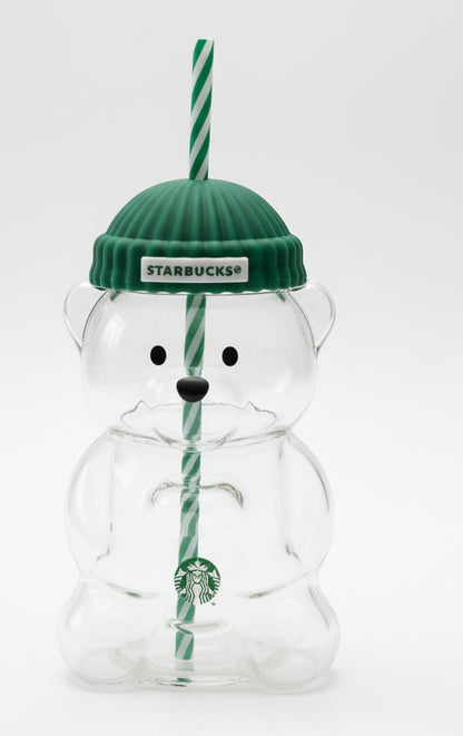 Clear bear-shaped tumbler with green knit cap and straw, featuring Starbucks logo, on a wooden surface.