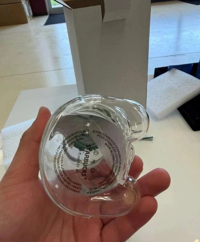Clear glass object with Starbucks logo held in a hand on a light-colored surface.