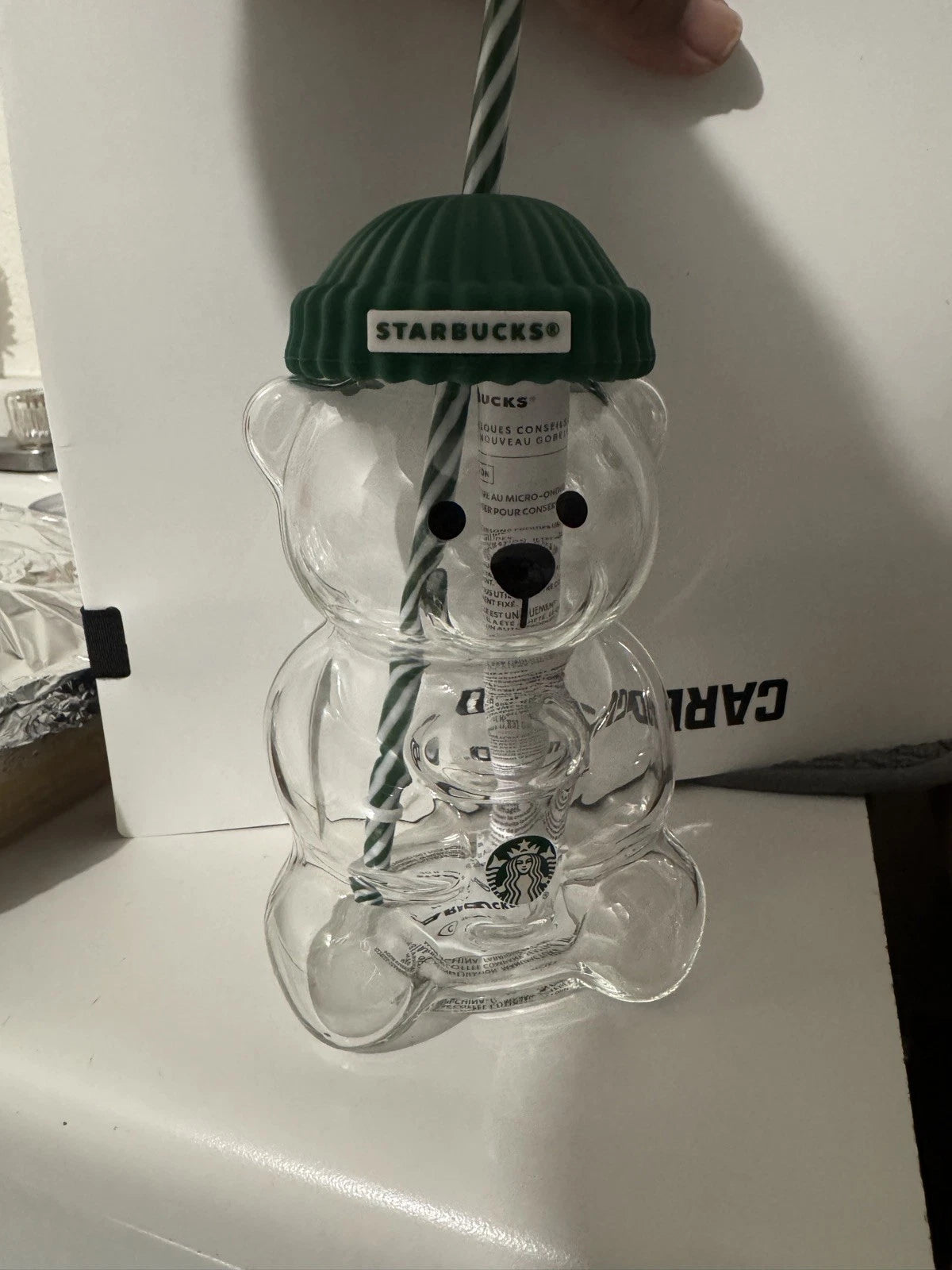 Clear bear-shaped cup with green lid and straw, featuring Starbucks branding, on a white surface.