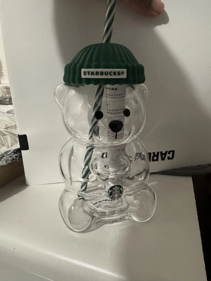 Clear bear-shaped cup with green lid and straw, featuring Starbucks branding, on a white surface.