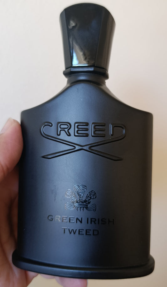 Black Creed perfume bottle held by a hand against a plain background