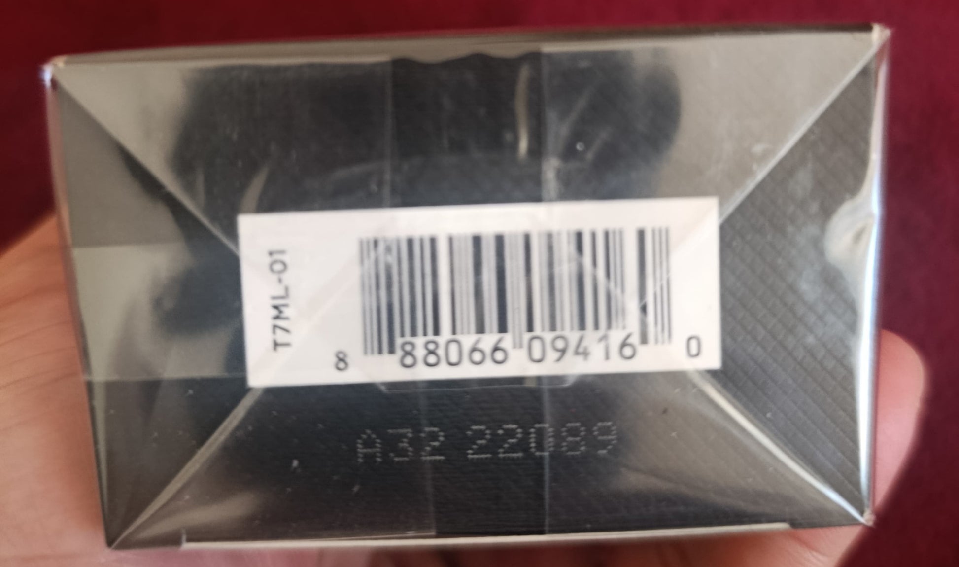 Silver rectangular object with a barcode label held in hand against a red background