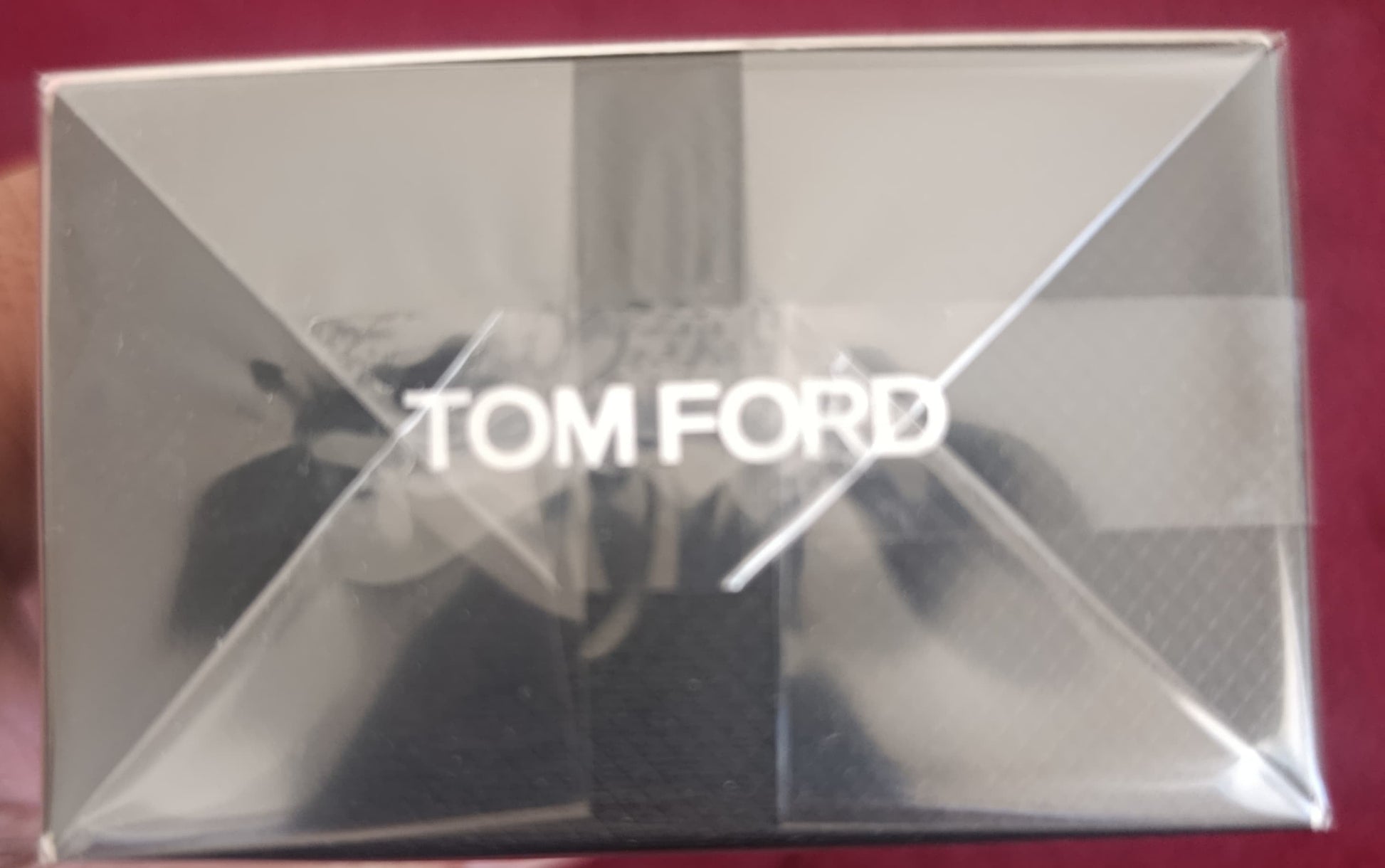 Tom Ford product packaging held by a hand on a red background