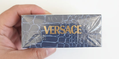 Versace product packaging held by a hand against a red background